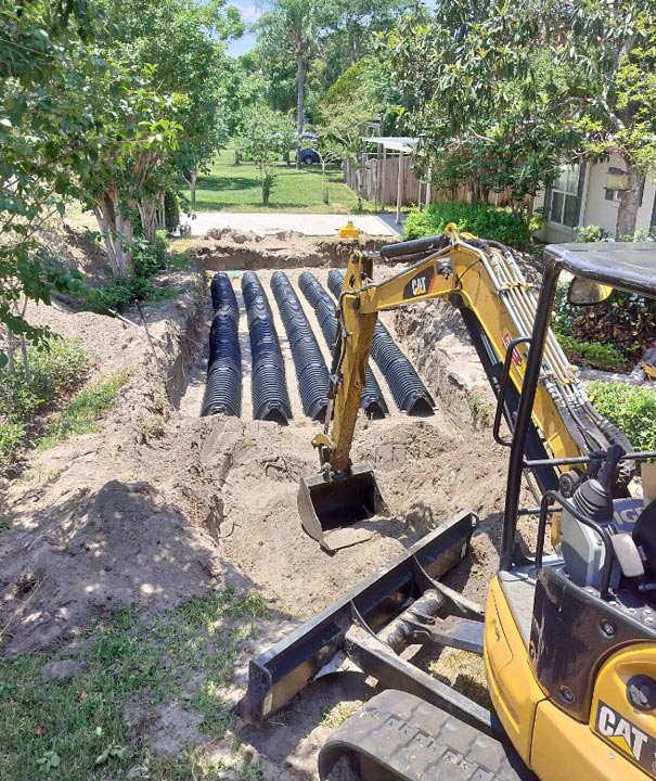 CAT mini excavator beside a new drain field of black pipe in a residential backyard