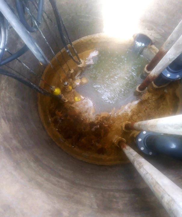 Lift station wet well before cleaning, with grease buildup and floating debris