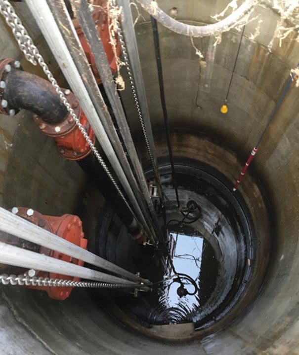 Inside a concrete lift station with red valves, pump guide rails and lifting chains